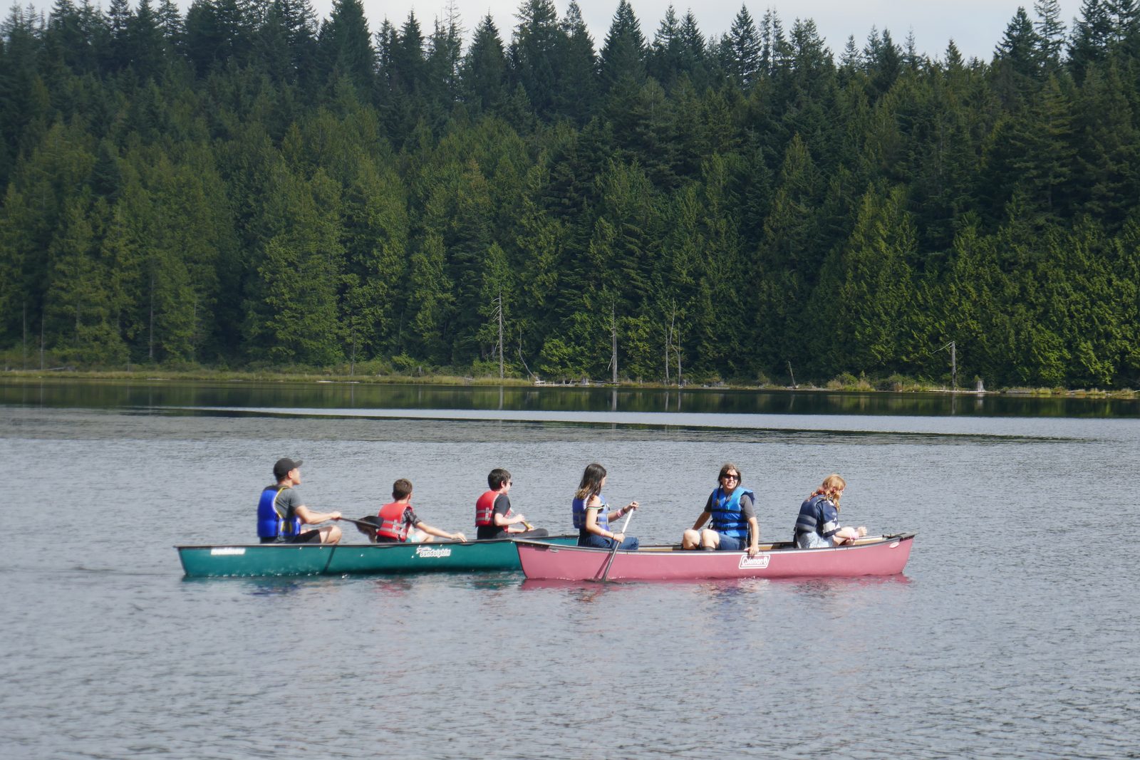 Students canoeing on a calm forest lake at camp